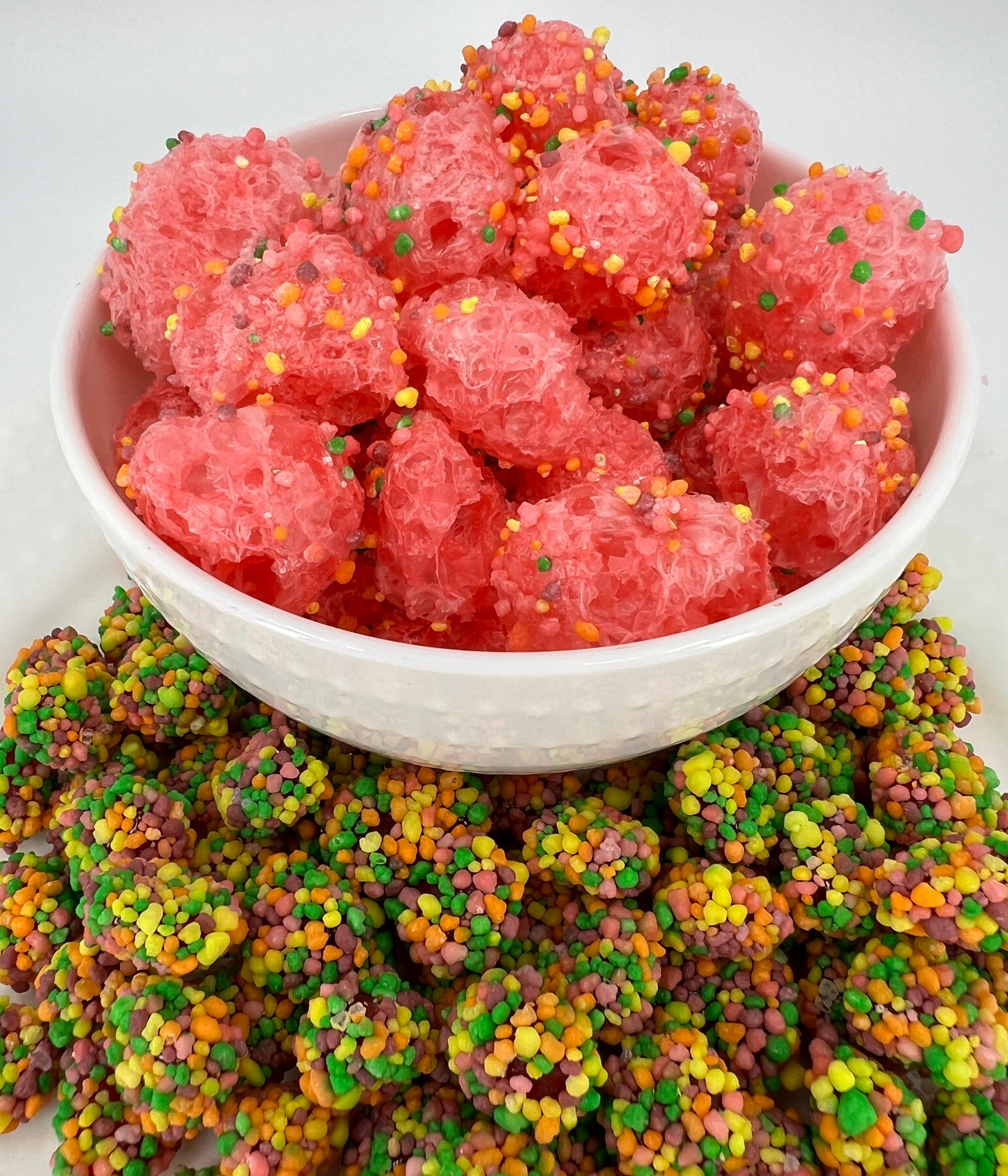 Pink gummy candies with colorful sprinkles in a white bowl on a white background