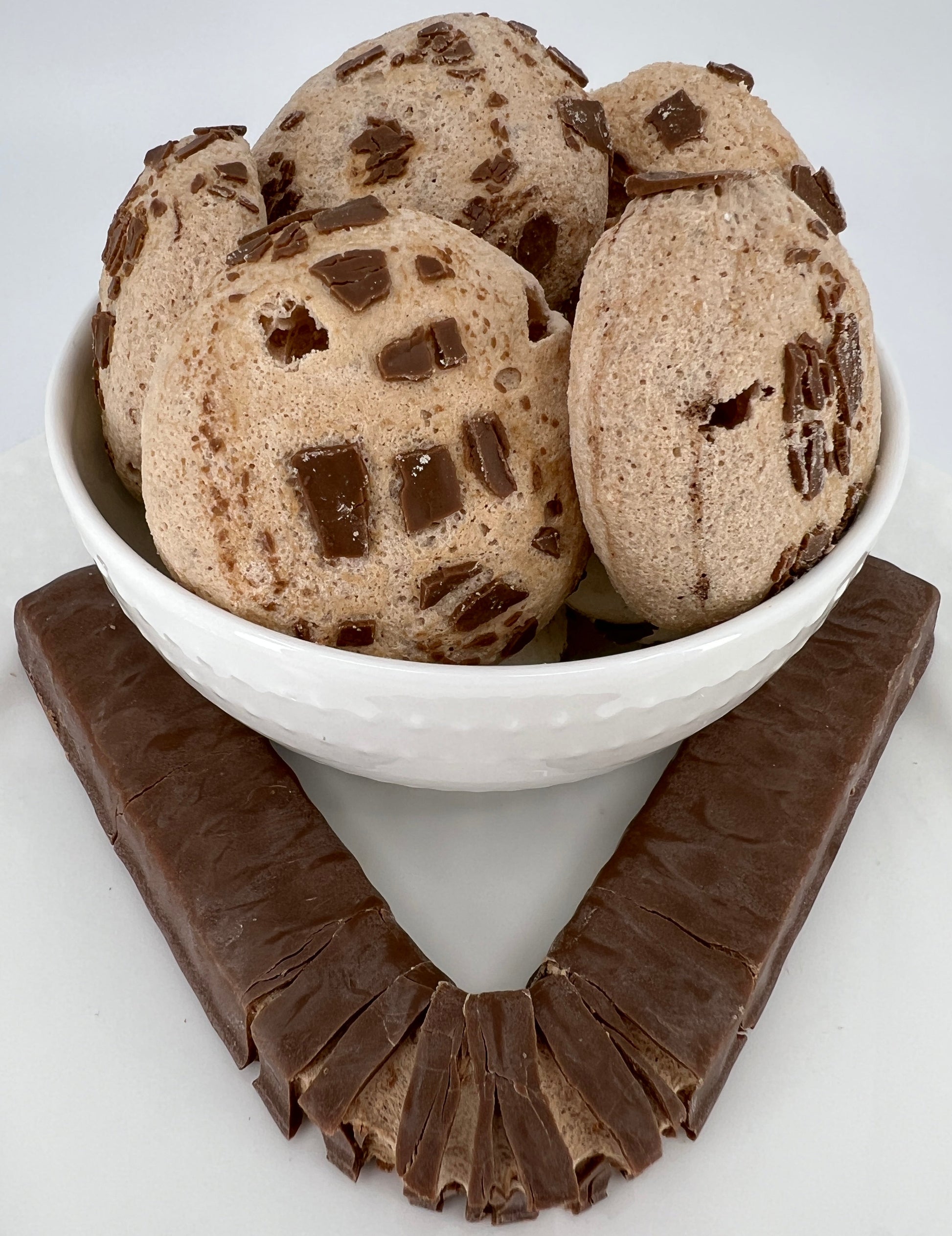 Chocolate chip cookies in a white bowl with a piece of chocolate on a white background