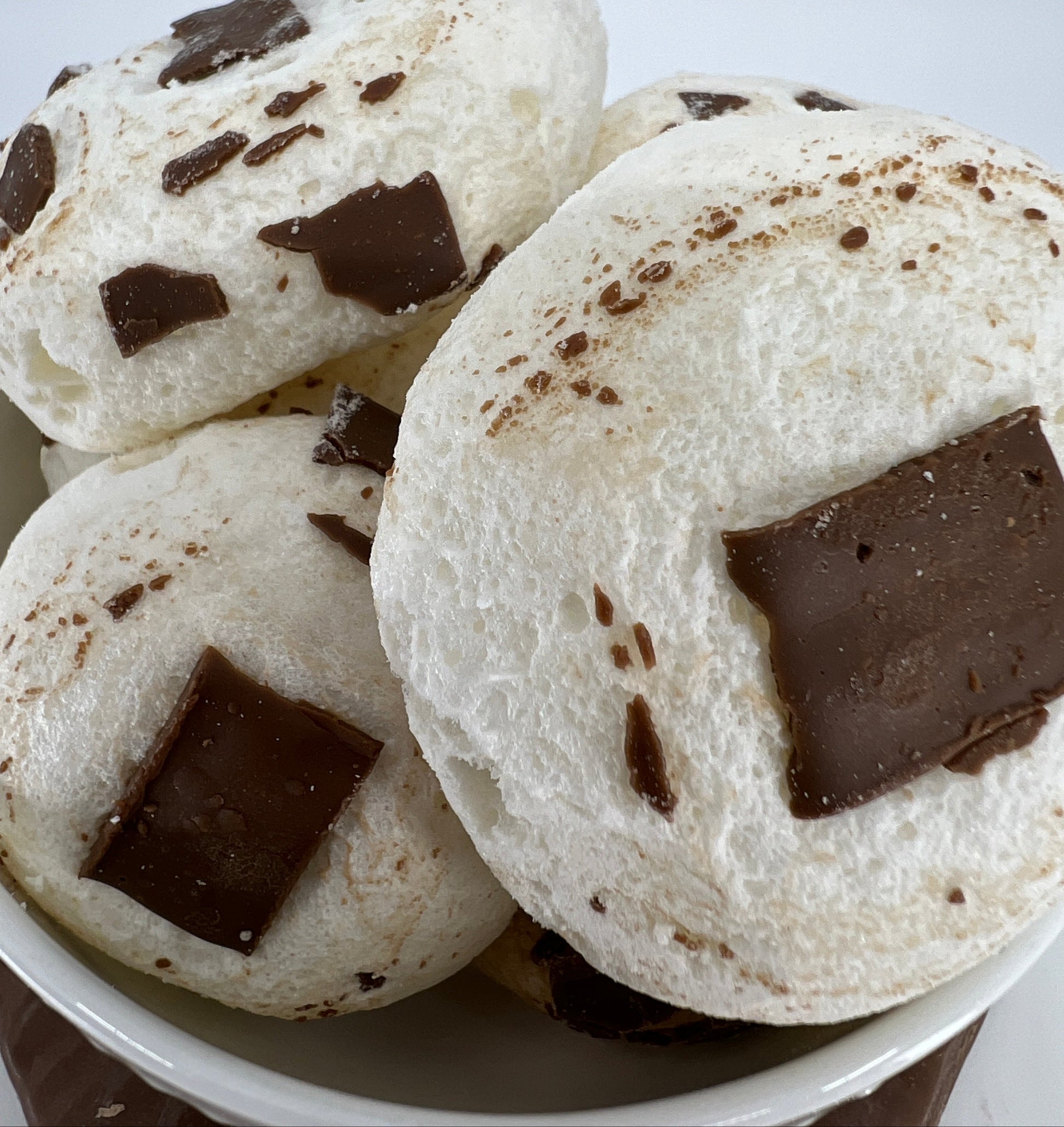 White cookies with chocolate chunks in a white bowl on a light gray background