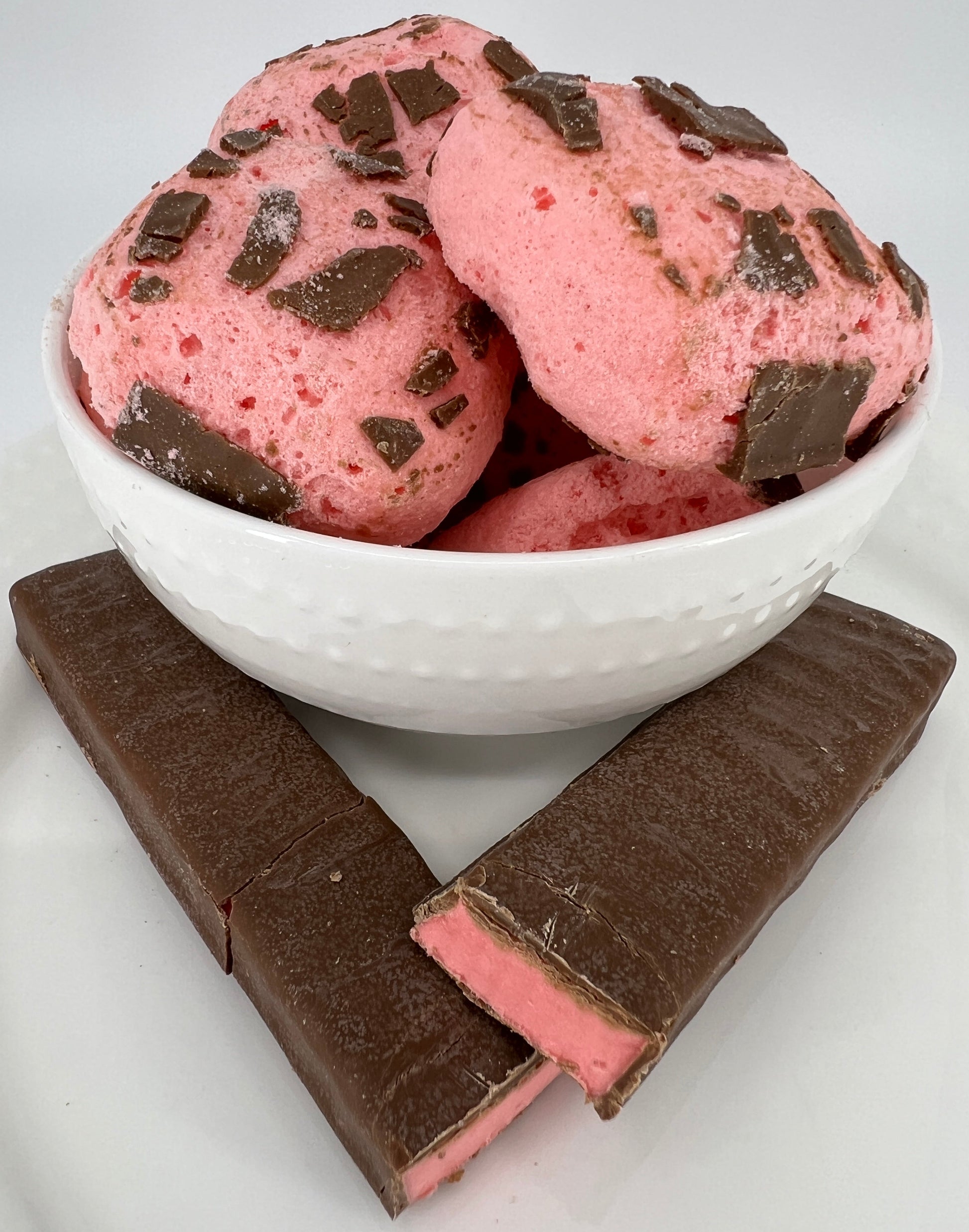 Pink chocolate pieces in a white bowl next to a chocolate bar on a light gray background