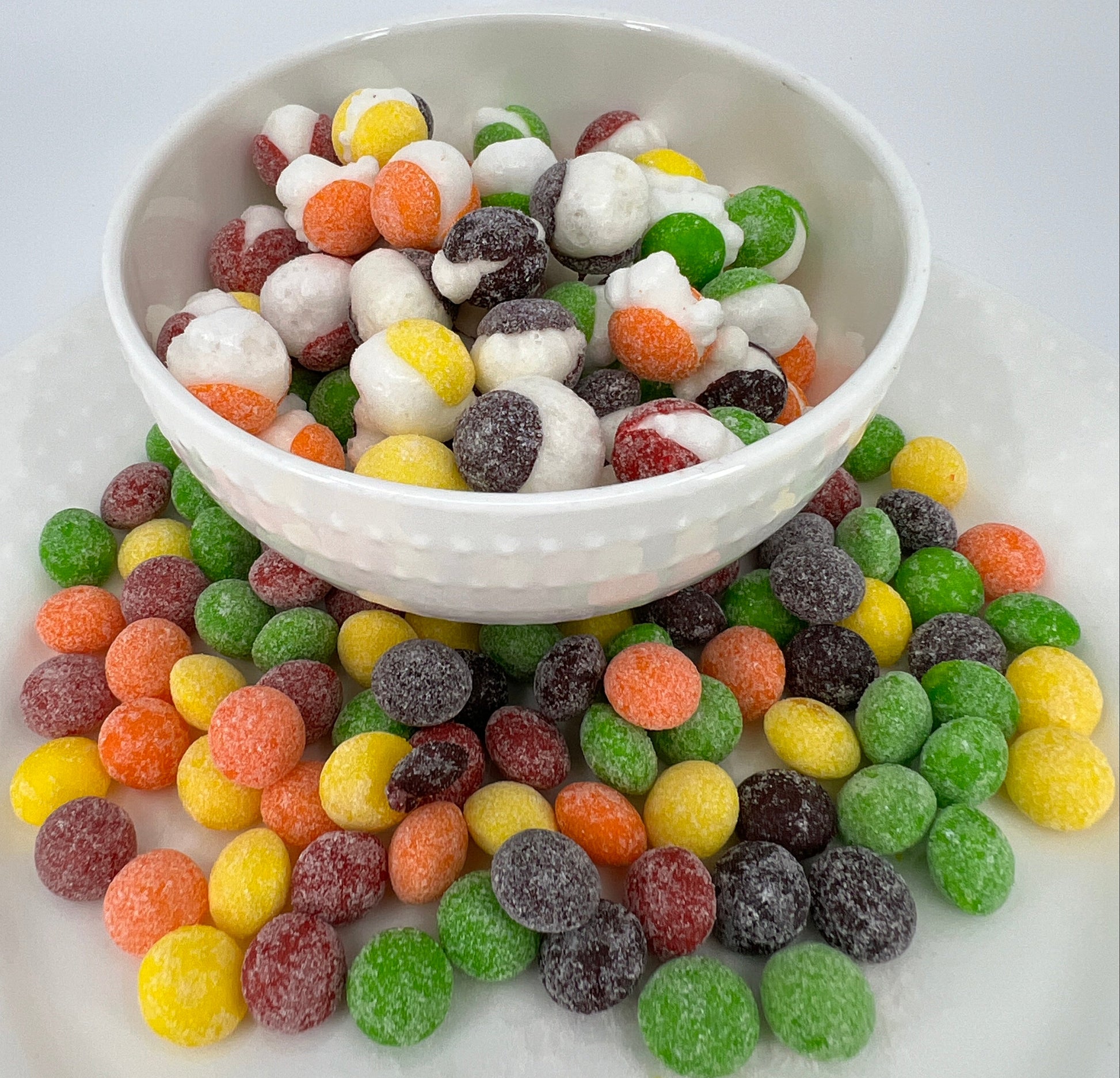 Colorful gummy candies spilling out of a white bowl on a light gray background