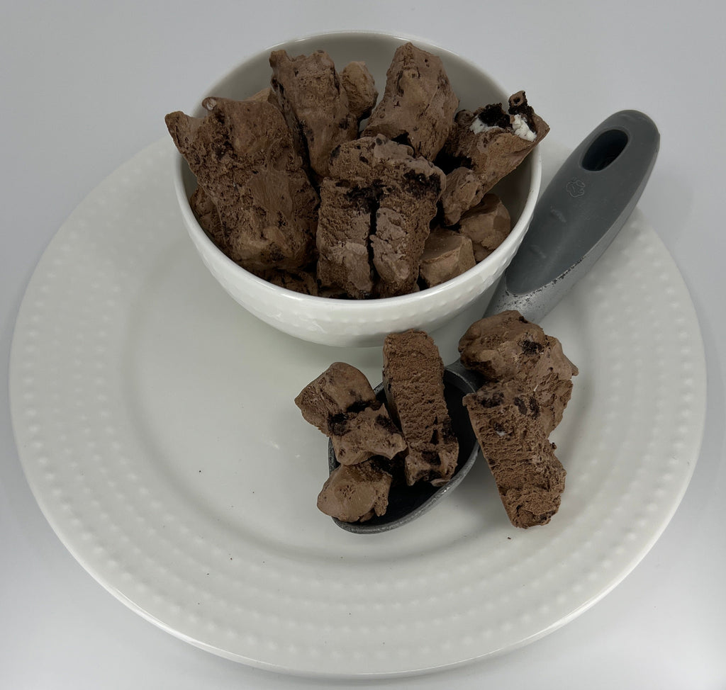 Bowl of chocolate ice cream on a white plate with a spoon on a light gray background