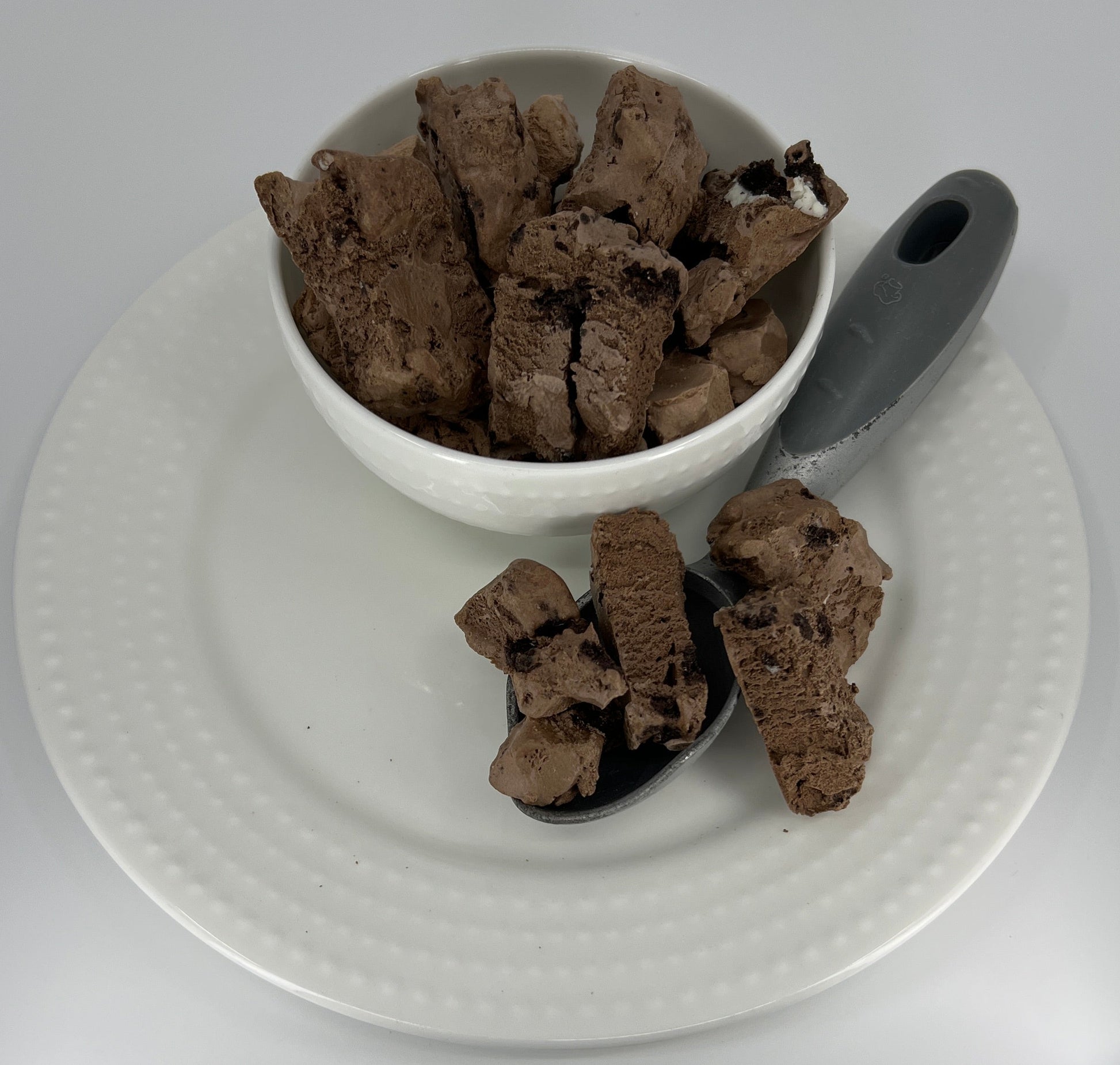 Bowl of chocolate ice cream on a white plate with a spoon on a light gray background