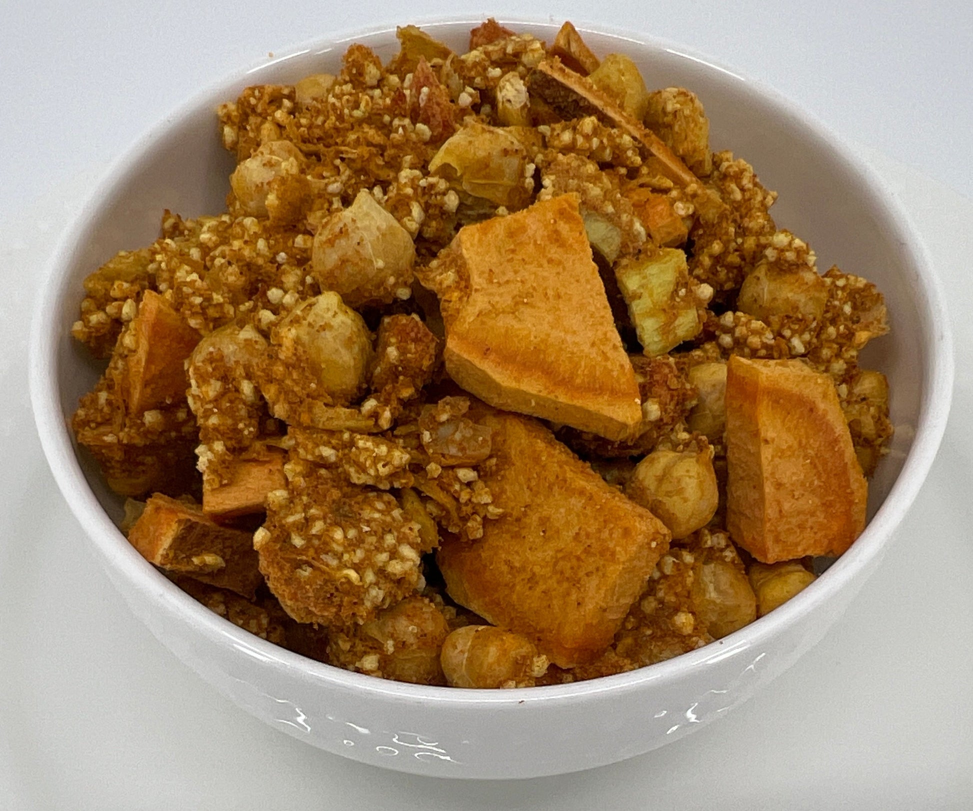 White bowl filled with a mix of nuts and cookies on a white plate